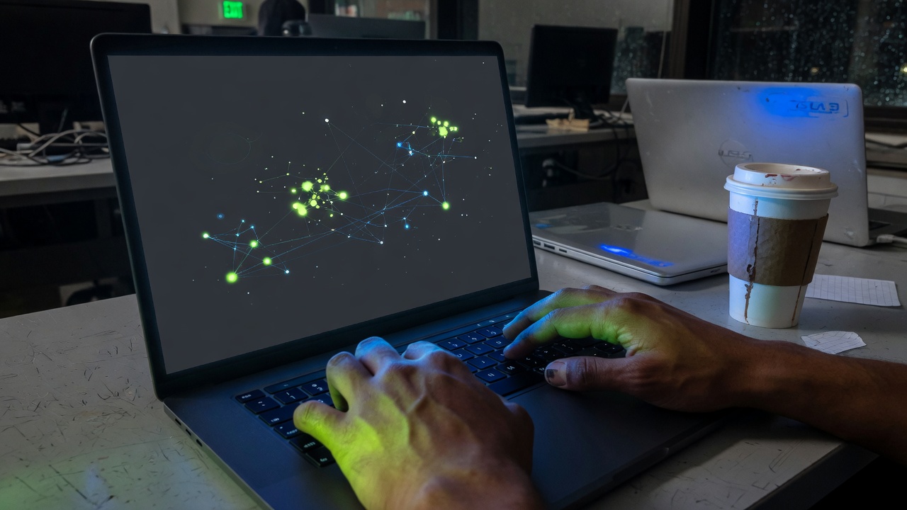 Hands on a Linux laptop showing a network graph in a campus lab at night